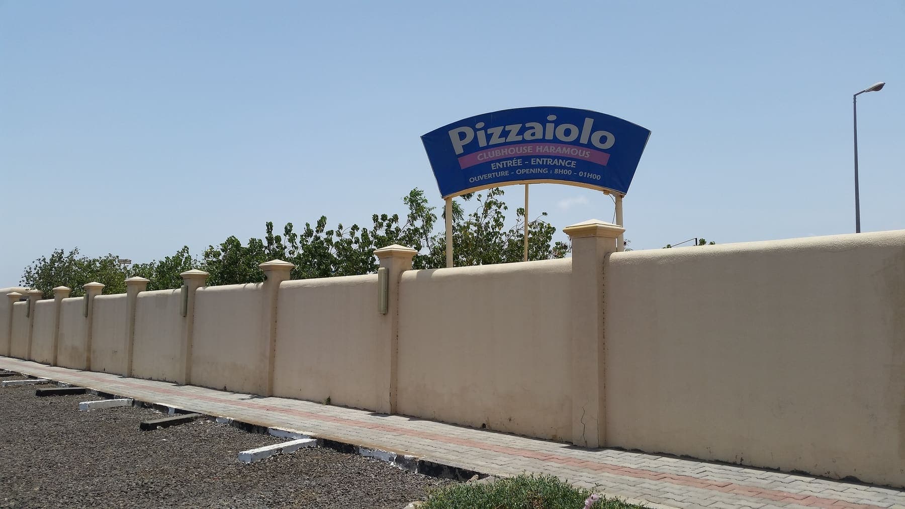 Rendered perimeter wall and paved verge along a Haramous street