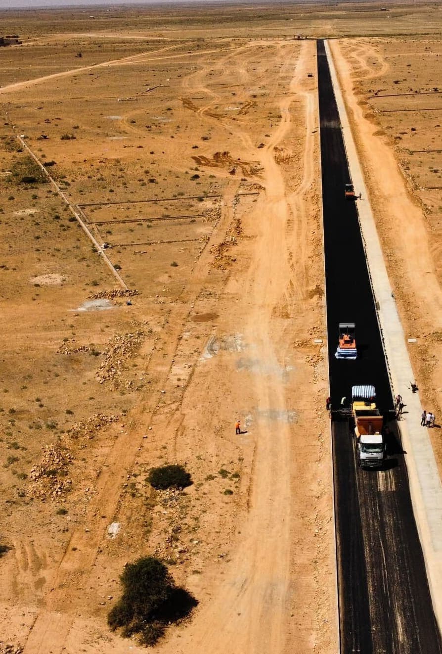 Aerial view of an asphalt paver and roller laying a new road through open ground